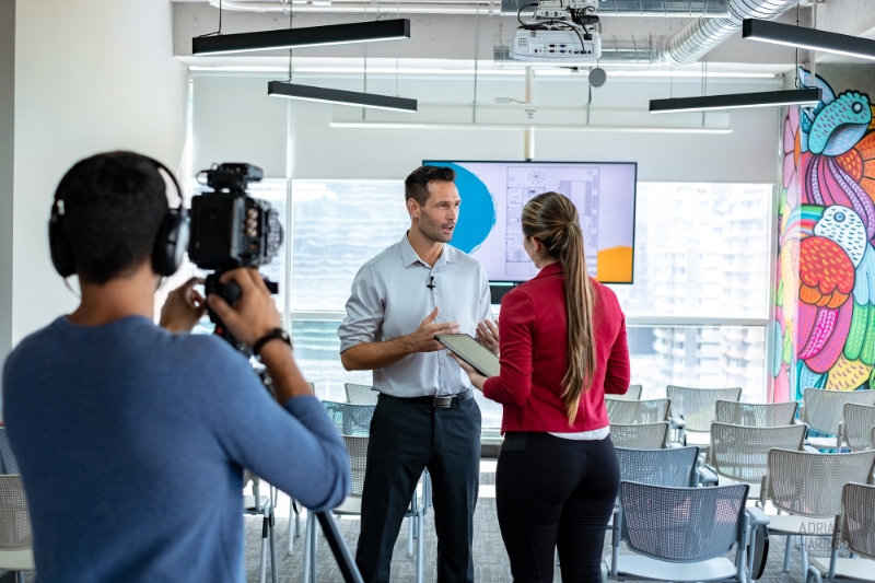 Behind the scenes of a corporate video shoot in Sydney. Man talking with female producer. Videographer holding camera filming.